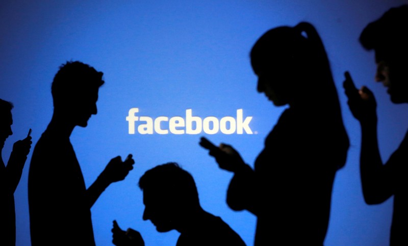 FILE PHOTO: People pose with mobile devices in front of projection of Facebook logo in this picture illustration taken in Zenica