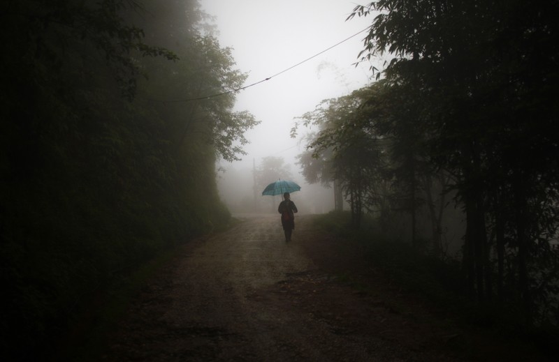 FILE PHOTO - A woman walks along a dirt road during a misty day in Sapa