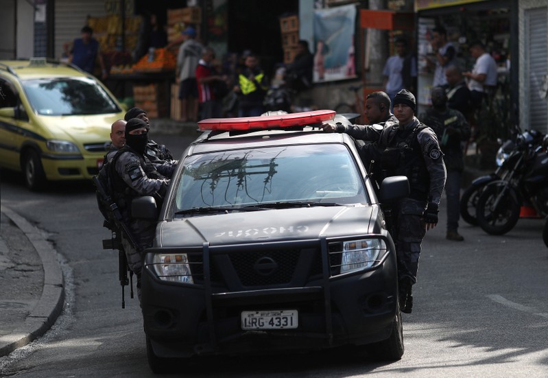 Police officers hang on to a car during an operation after clashes with drug dealers in Vidigal slum in Rio de Janeiro