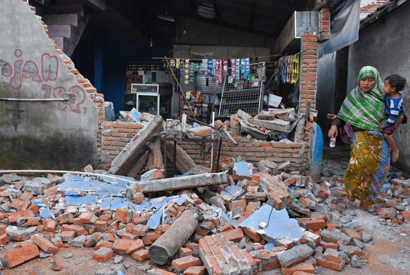 A woman walks past debris from a collapsed wall following a strong earthquake in Lendang Bajur Hamlet, Lombok