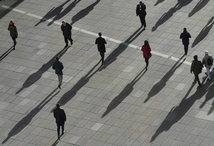 People cast long shadows in the winter sunlight as they walk across a plaza in the Canary Wharf financial district of London