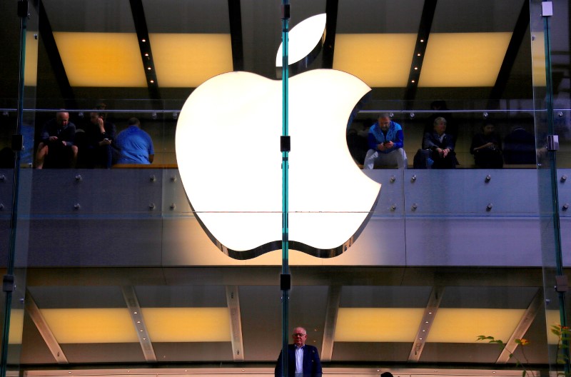 A customer stands underneath an illuminated Apple logo as he looks out the window of the Apple store located in central Sydney