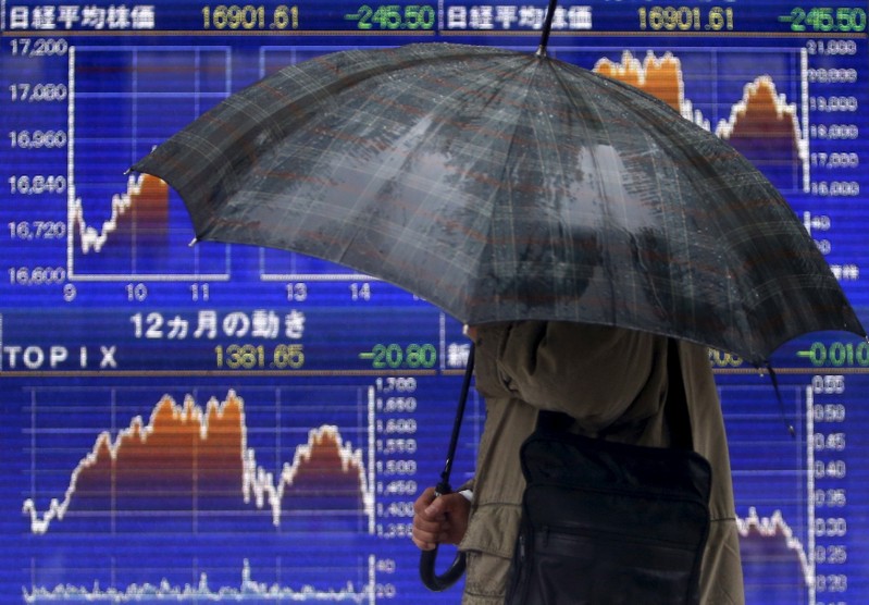 FILE PHOTO: A pedestrian holding an umbrella walks past an electronic board showing the graphs of the recent fluctuations of Japan's Nikkei average outside a brokerage in Tokyo