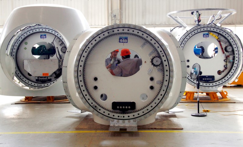 FILE PHOTO: Workers stand inside a newly painted wind turbine tower as a fan blows it dry, in an assembly workshop in Baoding