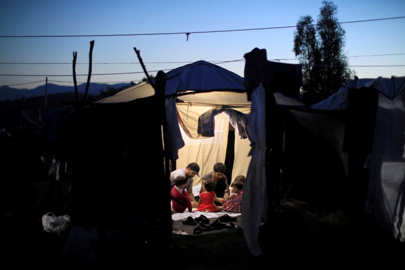 Two migrant men and four babies sit inside a tent at a makeshift camp next to the Moria camp for refugees and migrants on the island of Lesbos