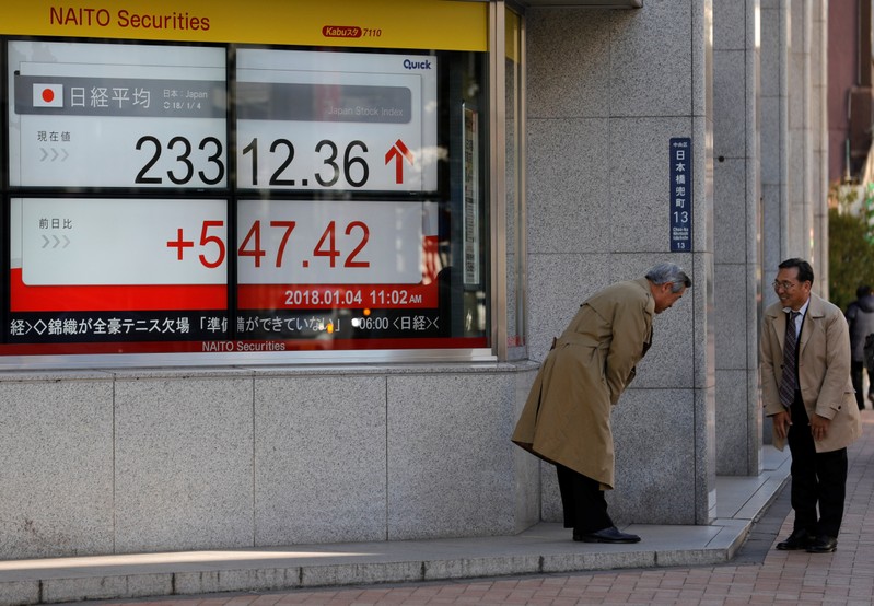 FILE PHOTO: Men exchange greetings in front of an electronic board displaying the Nikkei average outside a brokerage in Tokyo