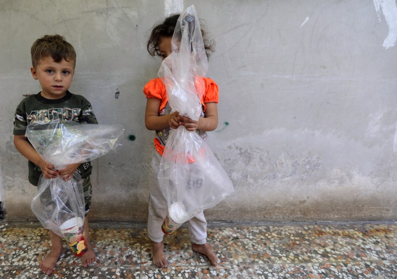 Children hold plastic bags with a paper cup in them, in Idlib