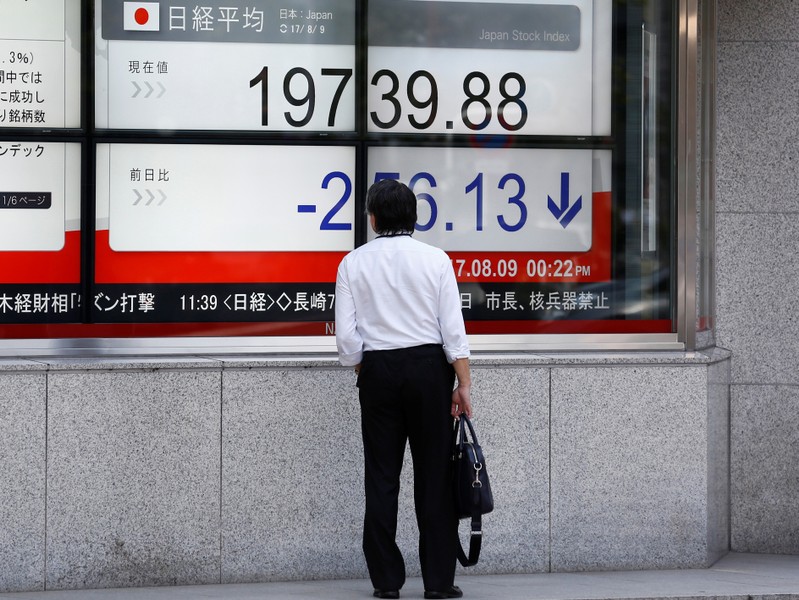 A man looks at an electronic board showing Japan's Nikkei average outside a brokerage at a business district in Tokyo