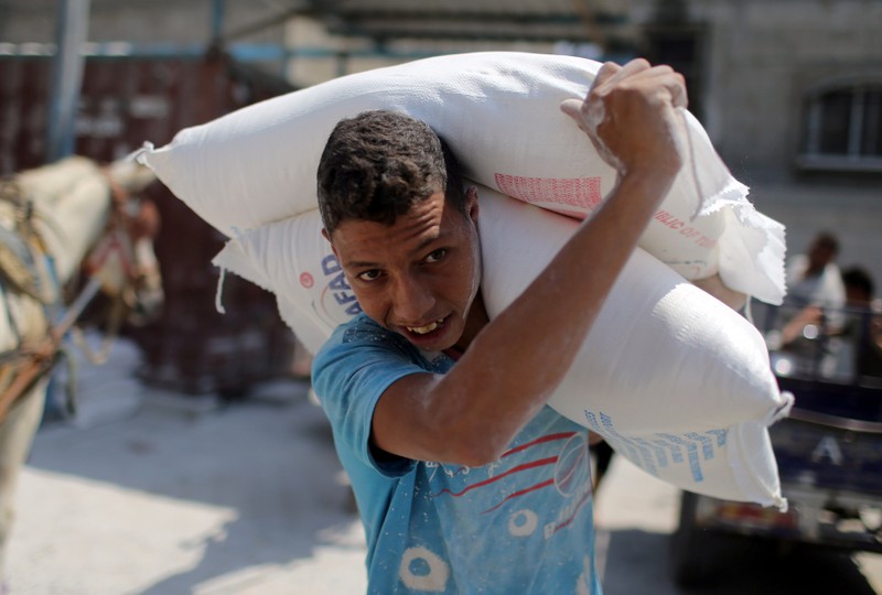 Palestinian carries bags of flour at an aid distribution center run by UNRWA, in Khan Younis in the southern Gaza Strip