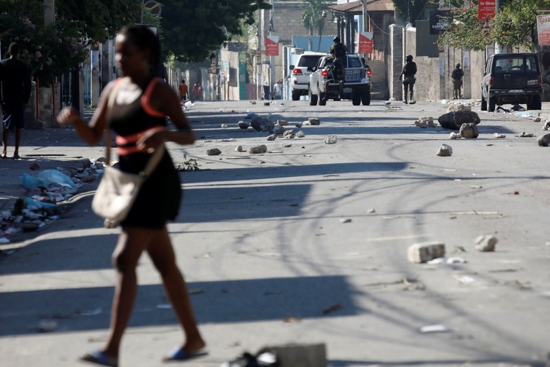 A woman walks in a street as Haitian National Police officers patrol after a march to demand an investigation into what they say is the alleged misuse of Venezuela-sponsored PetroCaribe funds, in Port-au-Prince