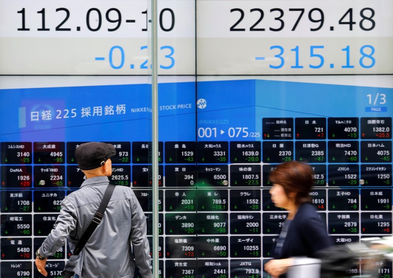 People walk past an electronic board showing Japan's Nikkei average and Japanese yen's exchange rate against the U.S. dollar outside a brokerage in Tokyo
