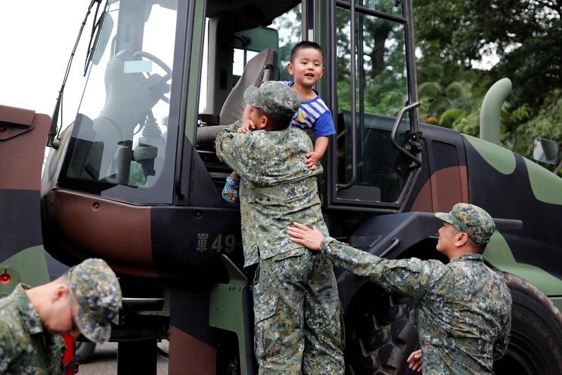A solider puts a child into a military vehicle during a public fair which displays military equipments, in Taipei