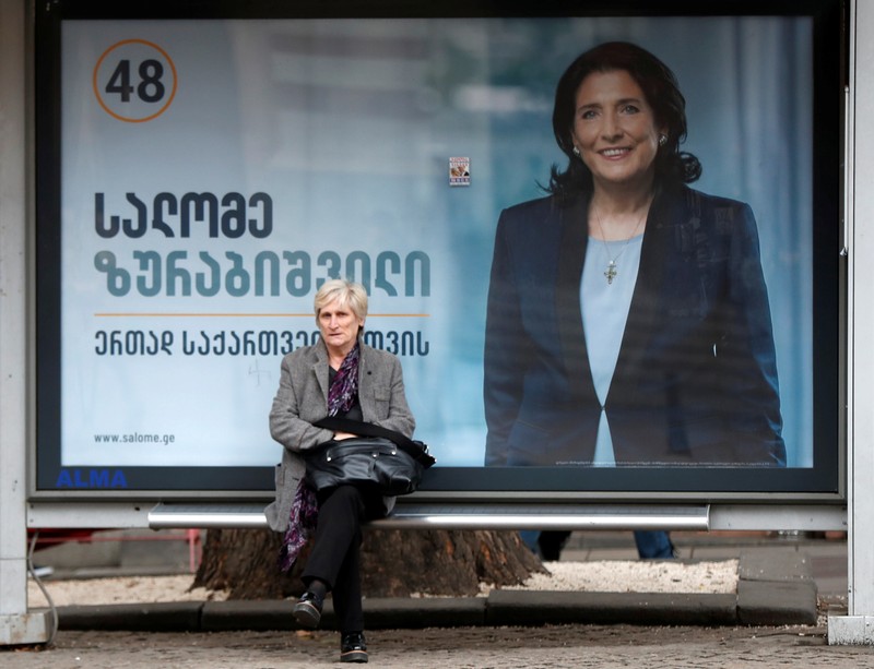 A woman sits at a bus stop decorated with a campaign poster of pro-government presidential candidate Salome Zurabishvili in Tbilisi