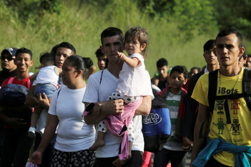 A man carries a child along other Hondurans fleeing poverty and violence, as they move in a caravan toward the United States, in San Pedro Sula