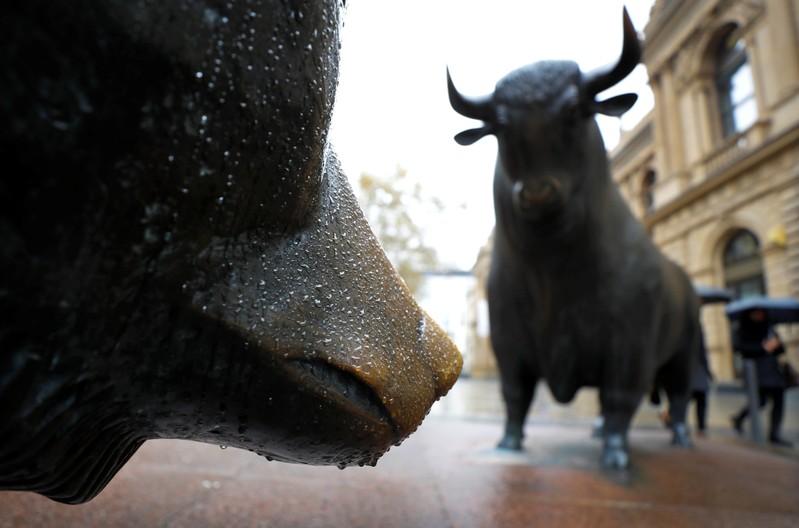 People with umbrellas pass by bull and bear outside Frankfurt's stock exchange during heavy rain in Frankfurt