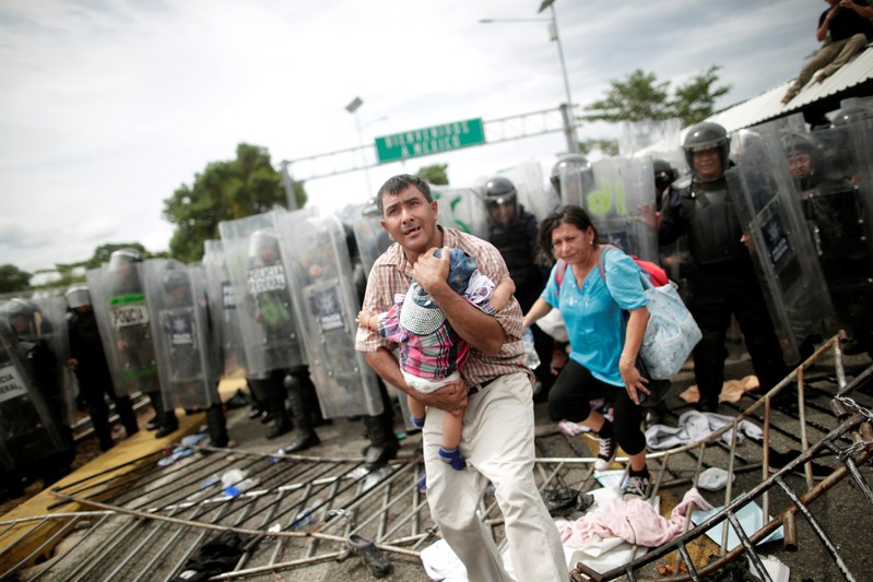 A Honduran migrant protects his child after fellow migrants, part of a caravan trying to reach the U.S., stormed a border checkpoint in Guatemala, in Ciudad Hidalgo