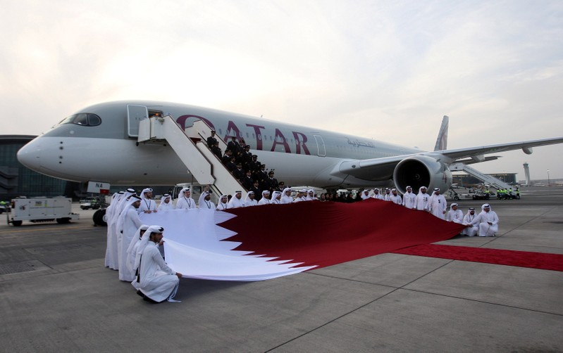 FILE PHOTO: Qatar Airways staff hold a Qatari flag in front of an Airbus A350-1000 at Hamad International Airport in Doha