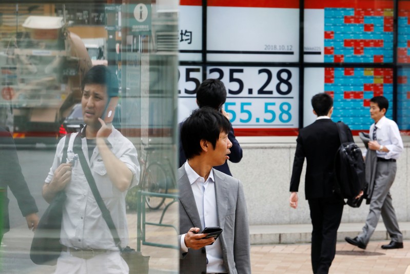 FILE PHOTO - People walk past an electronic board showing Japan's Nikkei average outside a brokerage in Tokyo