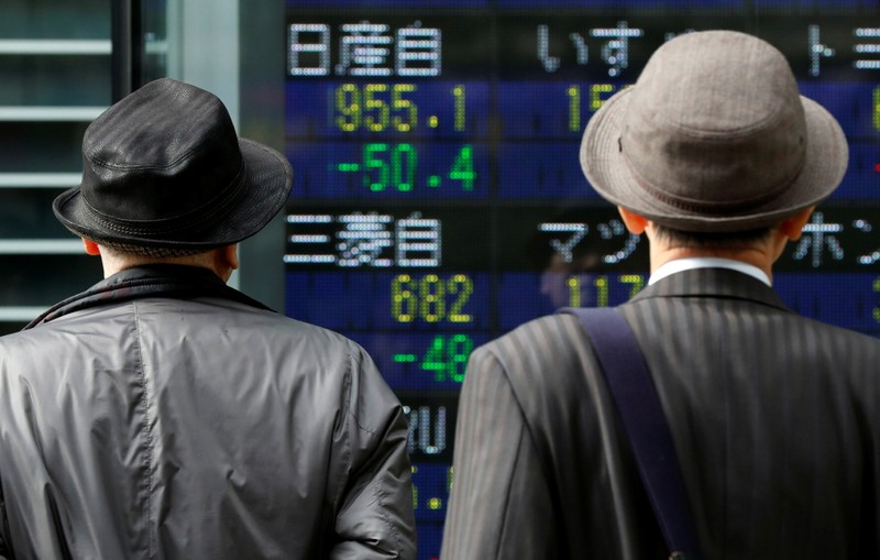 Men look at a stock quotation board showing share prices of Nissan Motor Co and Mitsubishi Motors outside a brokerage in Tokyo