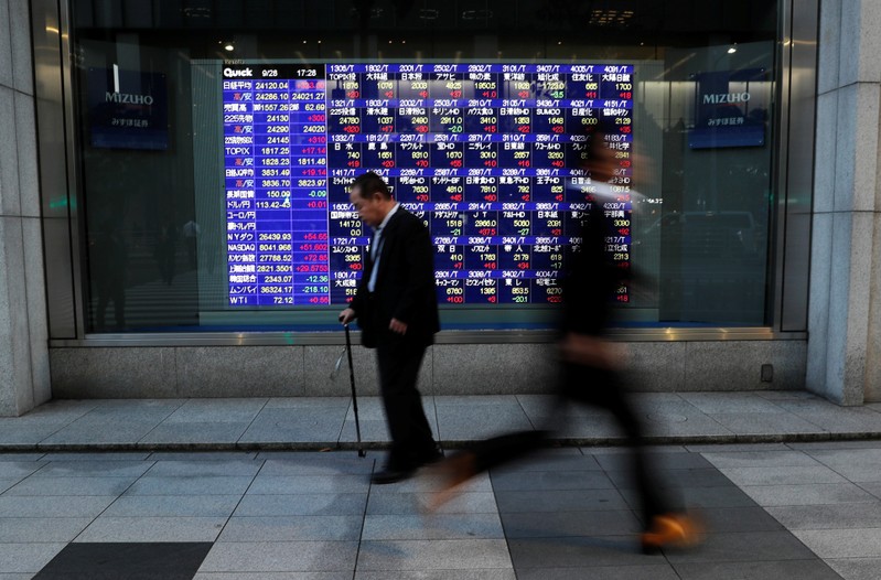 Passersby walk past in front of an electronic stock quotation board outside a brokerage in Tokyo
