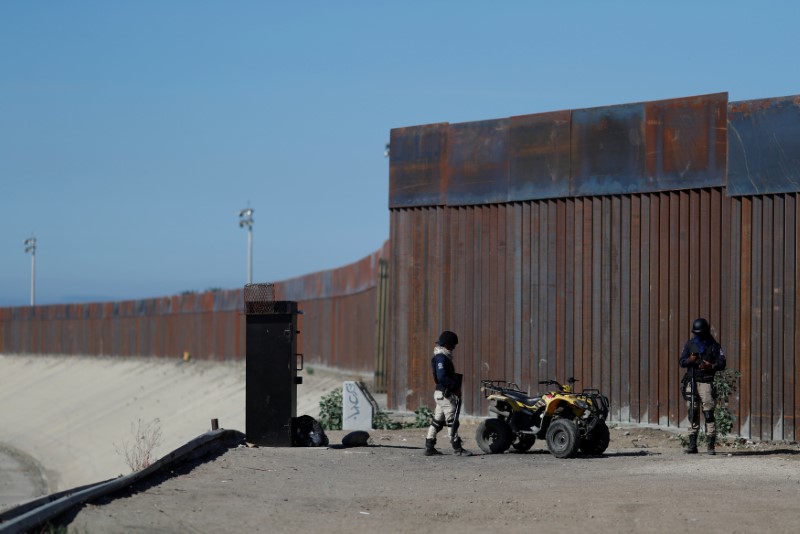Private security guards stand guard in front of the border fence between Mexico and United States, in Tijuana