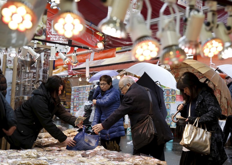 A vendor passes a plastic bag to a shopper at a food stall at a shopping district in Tokyo