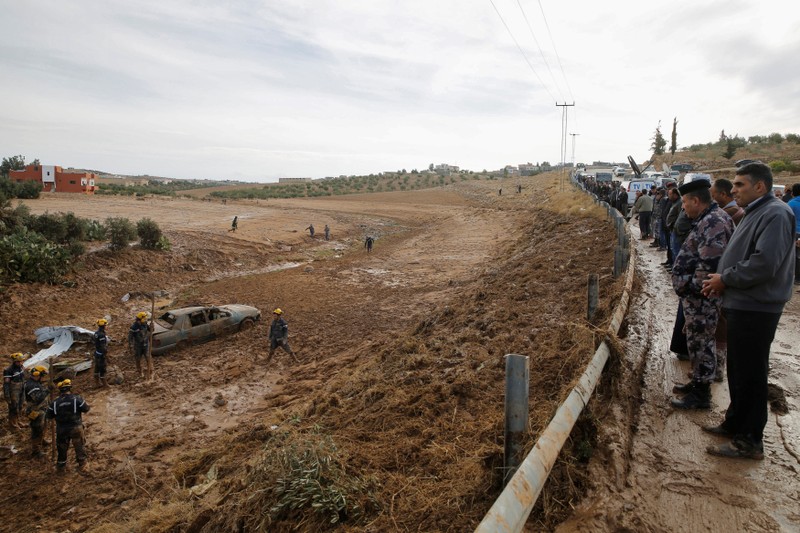 People watch civil defense members as they look for missing persons after rain storms unleashed flash floods, in Madaba city,
