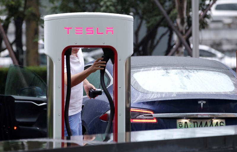 FILE PHOTO: A man finishes charging his Tesla car at a charging point outside Tesla China headquarters in Beijing