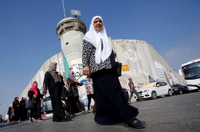 Palestinians pass by a section of the controversial Israeli barrier on their way to attend Friday prayer of the holy fasting month of Ramadan in Jerusalem's Al-Aqsa mosque, in Bethlehem in the occupied West Bank