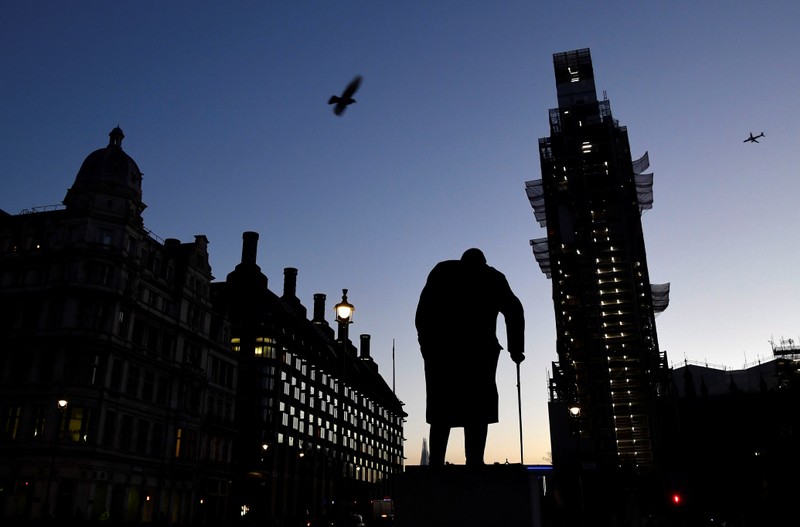 The sun comes up, silhouetting the statue of Churchill and Big Ben, in Westminster London