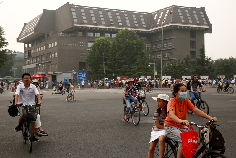 People cycle past a building in Peking University in Beijing