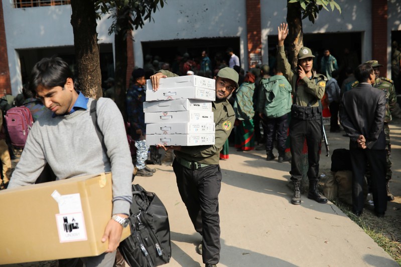 Law enforcement officials carry electronic voting materials as they distribute them to different voting centre ahead of 11th general election which will be held on December 30 in Dhaka