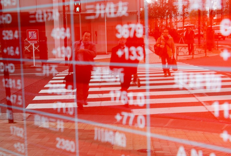 Pedestrians are reflected on an electronic board showing stock prices outside a brokerage in Tokyo