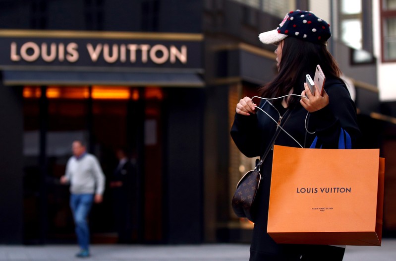 Woman with a Louis Vuitton-branded shopping bag looks towards the entrance of a branch store by LVMH Moet Hennessy Louis Vuitton in Vienna