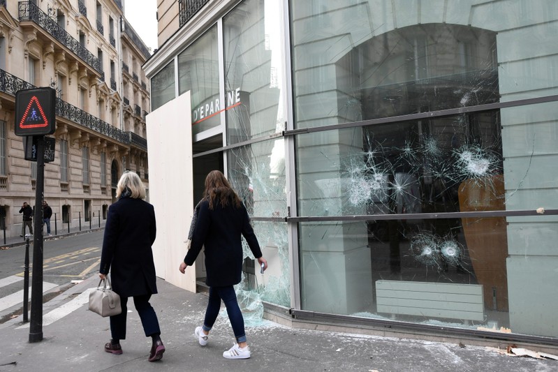 People walk by a vandalized savings bank window the day after clashes during a national day of protest by the 