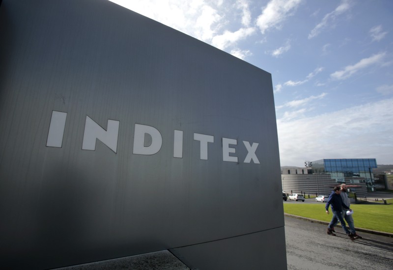 FILE PHOTO: Men walk by an Inditex logo at the entrance of a Zara factory, the headquarters of Inditex group, in Arteixo
