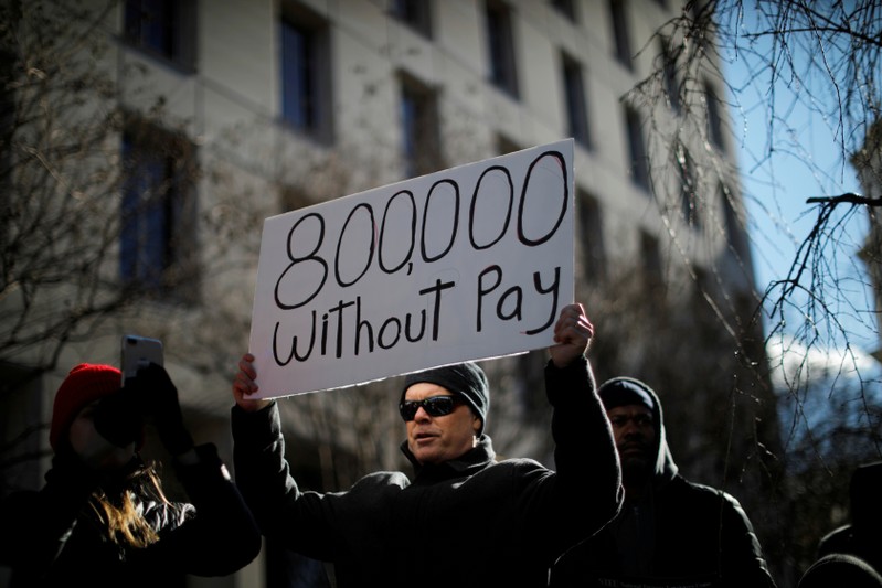 FILE PHOTO: A demonstrator holds a sign, signifying hundreds of thousands of federal employees who won’t be receiving their paychecks as a result of the partial government shutdown