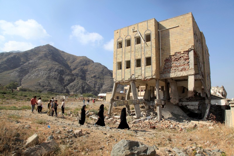 People walk past a school, damaged during the ongoing war in Taiz