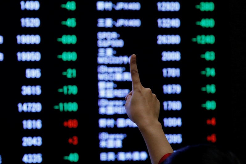 FILE PHOTO: A woman points to an electronic board showing stock prices as she poses in front of the board after the New Year opening ceremony at the Tokyo Stock Exchange (TSE), held to wish for the success of Japan's stock market, in Tokyo