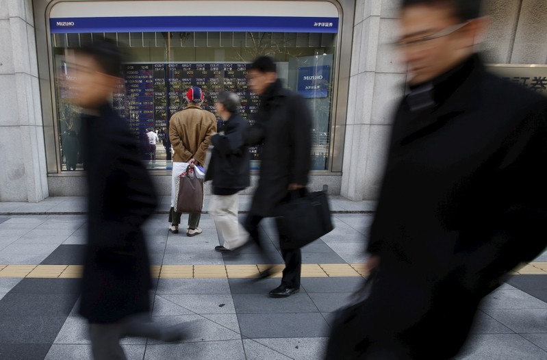 FILE PHOTO - A pedestrian looks at various stock prices outside a brokerage in Tokyo