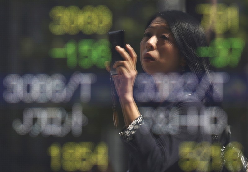 FILE PHOTO - A woman using a smartphone is reflected on a stock quotation board outside a brokerage in Tokyo, Japan