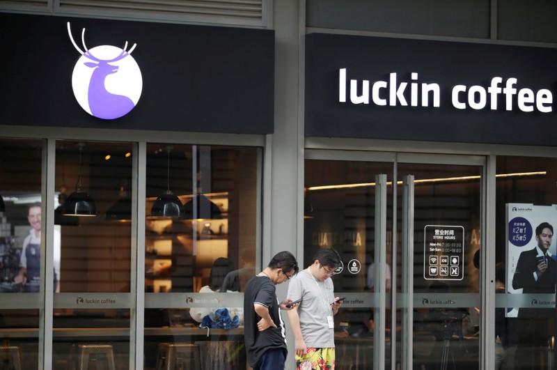 Men check their mobile phones outside a Luckin Coffee store in Beijing