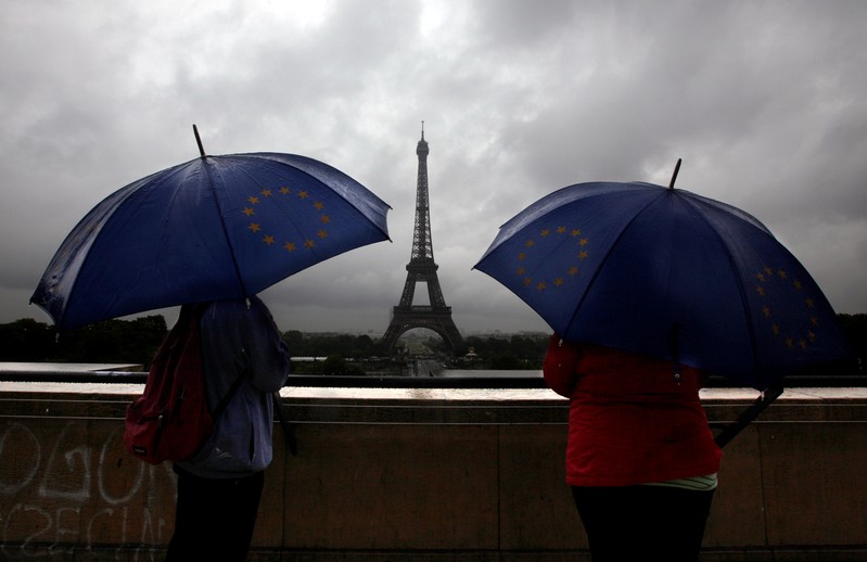 Tourists protect themselves from the rain under umbrellas in front of the Eiffel tower as they visit the French capital during summer holidays in Paris