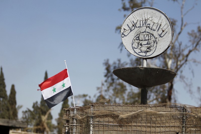 FILE PHOTO: A file photo of a Syrian national flag fluttering next to the Islamic State's slogan at a roundabout where executions were carried out by ISIS militants in the city of Palmyra