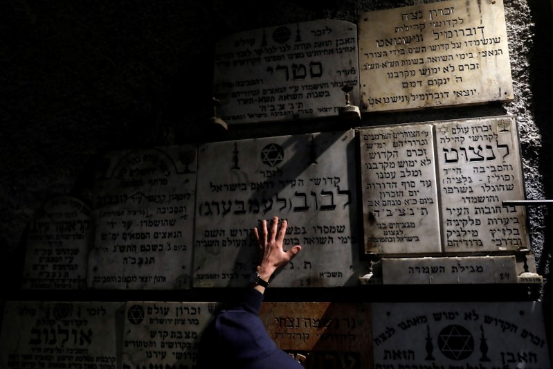 A man touches a gravestone commemorating the Jewish villages and towns whose communities were wiped out by the Nazis, inside 