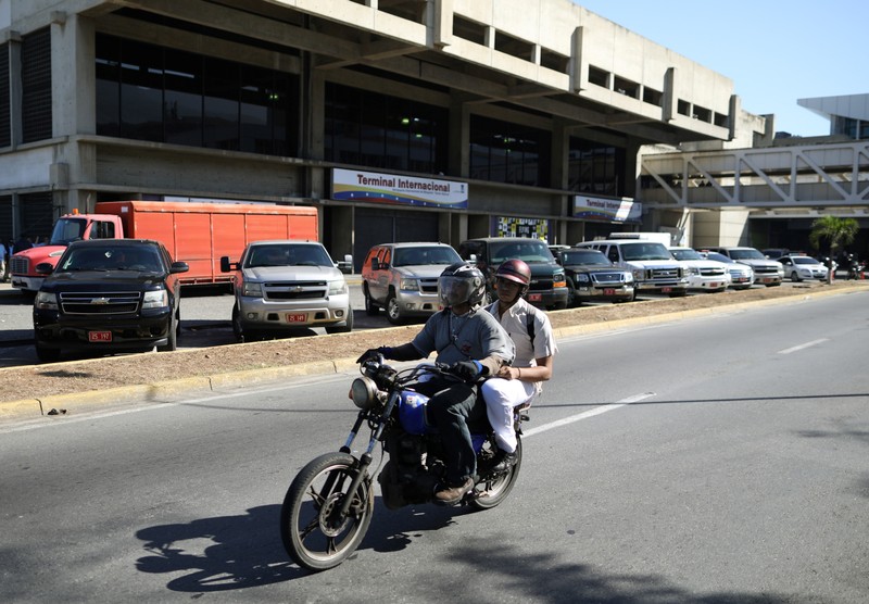 People on a motorcycle ride past vehicles with diplomatic licence plates parked outside the international terminal at the Simon Bolivar International Airport in Caracas