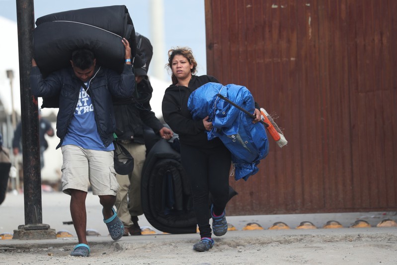 A migrant man and woman, part of a caravan of thousands from Central America tying to reach the United States, carry their belongings during the closing of the Barretal shelter in Tijuana, Mexico