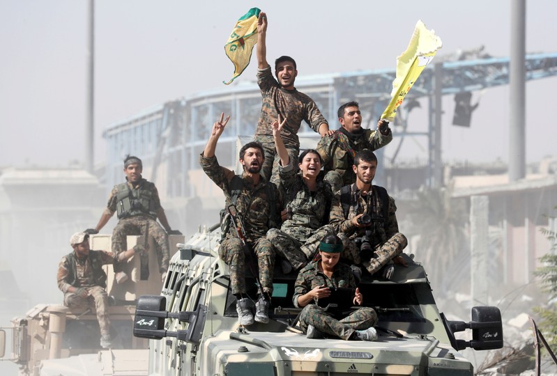 FILE PHOTO: Kurdish-led militiamen ride atop military vehicles as they celebrate victory over Islamic State in Raqqa