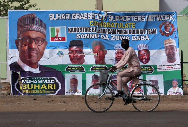 A cyclist drives pasts a campaign poster for President Muhammadu Buhari in a street after the postponement of the presidential election in Kano