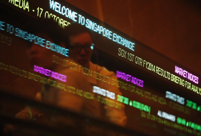 FILE PHOTO - People pass stock index tickers at the Singapore Exchange (SGX) premises